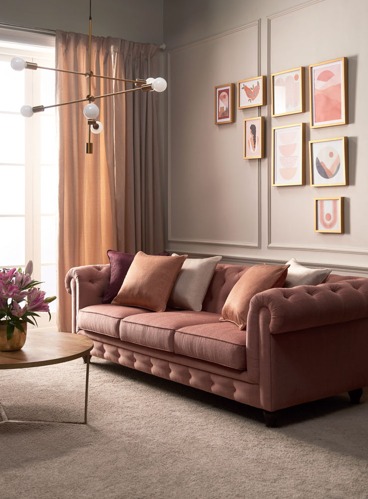 Room with a pink sofa, hanging golden light, and a wall with frames hung on it