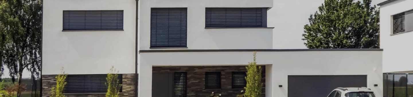 A home exterior with glass windows, white walls, and trees surrounding the home
