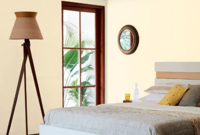 A bedroom painted with Pale Sisal Shade walls, a bed by a wooden window with a lampshade and mirror on the wall