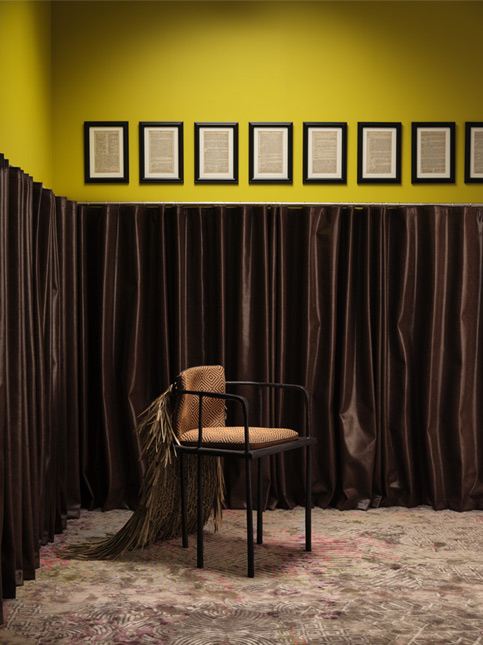 A chair with decorative elements against dark curtains and a yellow wall with framed art - Beautiful Homes