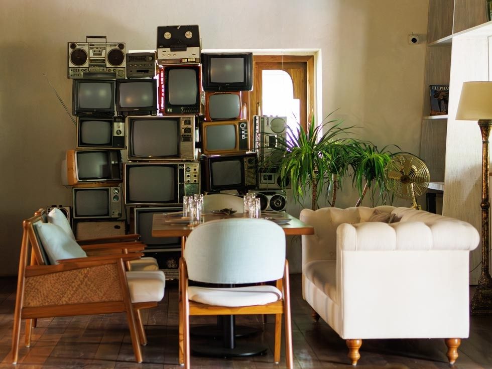 A modern rustic lounge with wooden interiors, pastel seating, and a vintage TV wall centerpiece - Beautiful Homes