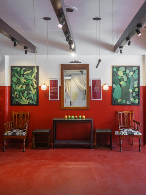 A vibrant red room with two framed botanical prints, a central mirror, and antique wooden furniture - Beautiful Homes