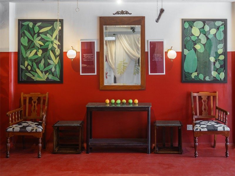 A vibrant red room with two framed botanical prints, a central mirror, and antique wooden furniture - Beautiful Homes