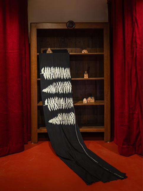 A black fabric with white fern-like patterns drapes from a wooden bookshelf - Beautiful Homes
