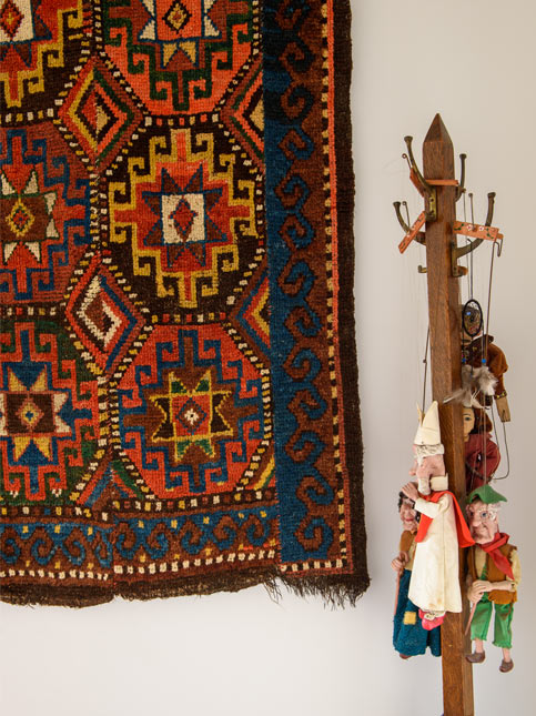 A vividly patterned tapestry hangs beside a wooden stand adorned with whimsical marionette puppets, blending folk art with traditional textile design - Beautiful Homes