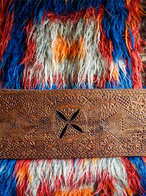 A close-up of a vibrantly coloured rug backdrop paired with an intricately carved wooden panel - Beautiful Homes