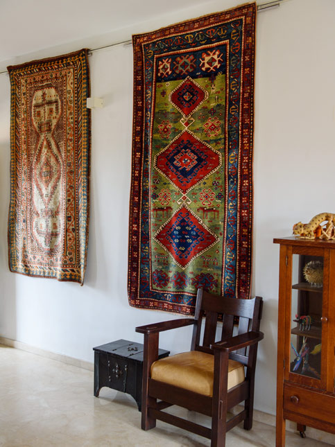 A wall corner with traditional rugs on the wall, a wooden armchair, and a display cabinet showcasing eclectic décor - Beautiful Homes