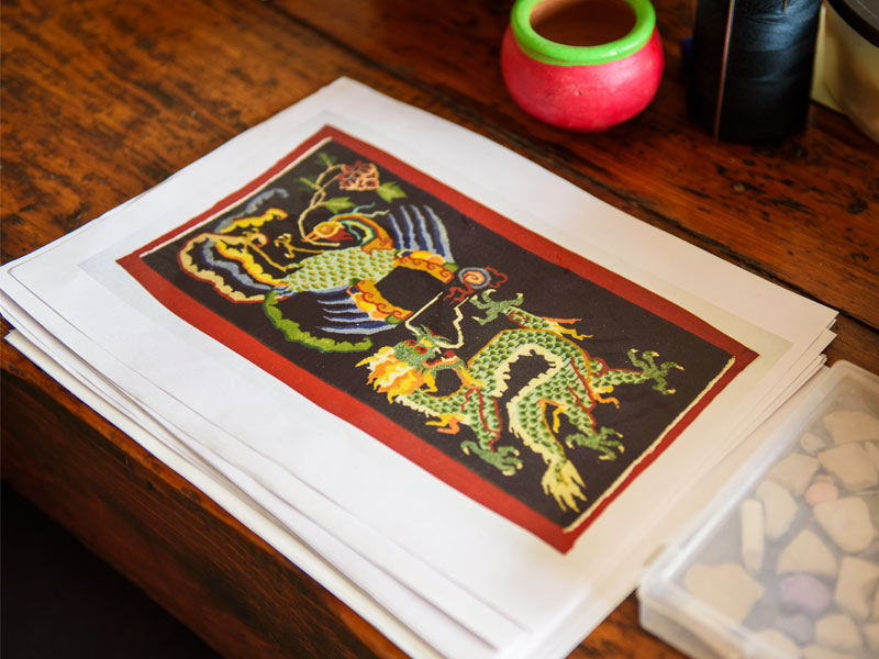 A stack of printed papers featuring a vibrant dragon illustration lies on a rustic wooden table surrounded by art supplies and tools - Beautiful Homes