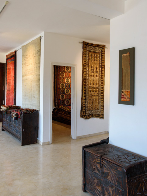 A gallery-like space displays intricately patterned rugs and vintage wooden chests with rustic decor - Beautiful Homes