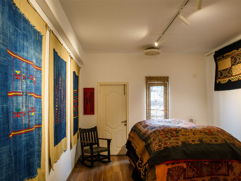 A room featuring stacked embroidered rugs on walls and bed, a wooden rocking chair - Beautiful Homes