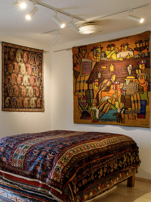 A cozy room adorned with vibrant woven wall rugs and a richly patterned bedspread - Beautiful Homes