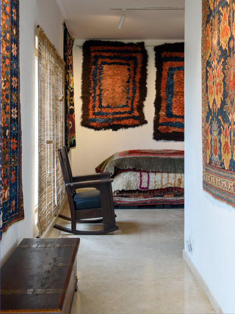 A cozy room adorned with traditional rugs on the walls and bed, featuring a wooden rocking chair and natural bamboo blinds - Beautiful Homes