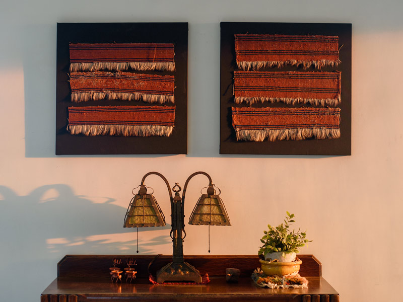 Two framed textile artworks hang above a wooden table with a vintage lamp and a potted plant - Beautiful Homes