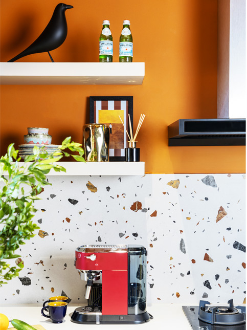 A modern kitchen with a red coffee machine, a white and multi-coloured speckled backsplash, and orange walls – Beautiful Homes