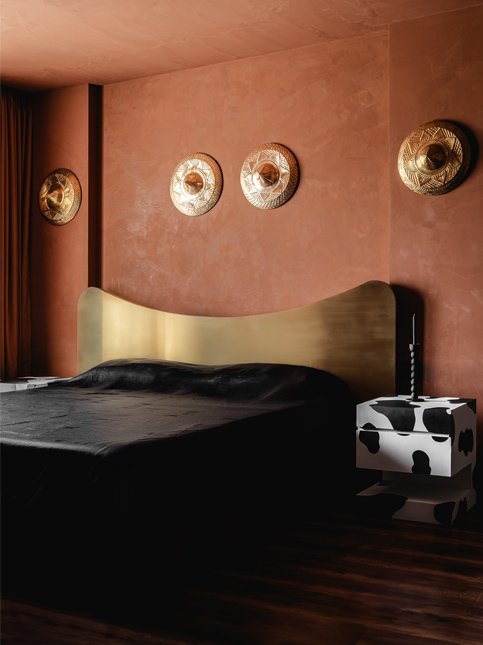 Warm bedroom with terracotta walls, a brass headboard, and decorative elements inspired by Assamese roots, creating a sense of familiarity – Beautiful Homes