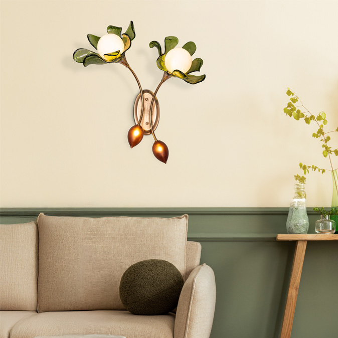 A flower-shaped wall sconce with green glass petals and white bulbs illuminates a cozy room with a beige sofa and a wooden console table – Beautiful Homes