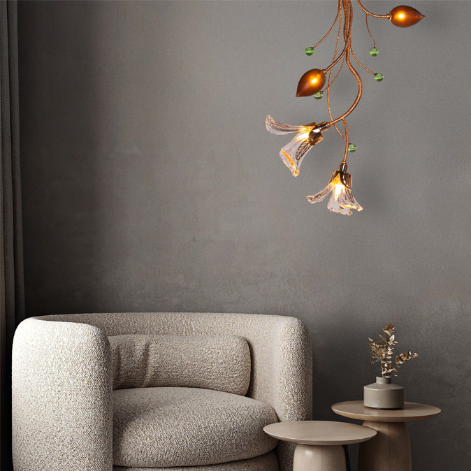 An artistic light fixture with glass flower shades and amber bulbs hangs above a cream armchair and two round side tables in a minimalist room – Beautiful Homes