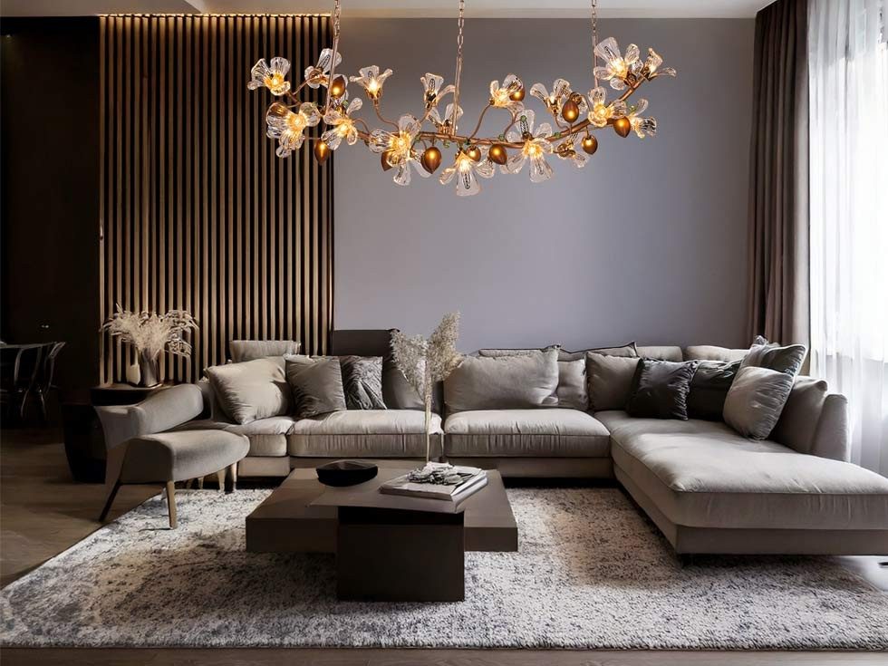 A large, ornate chandelier with crystal flowers and amber lights hangs above a modern living room with a sectional sofa and dark wood accents – Beautiful Homes