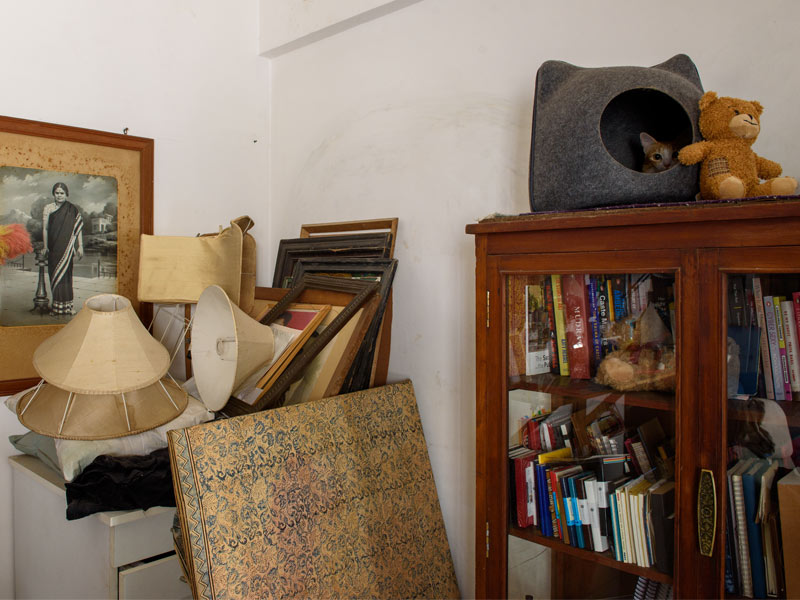 Corner with Stacked Artworks, Lampshades, and a Bookshelf with a Cat Bed – Beautiful Homes