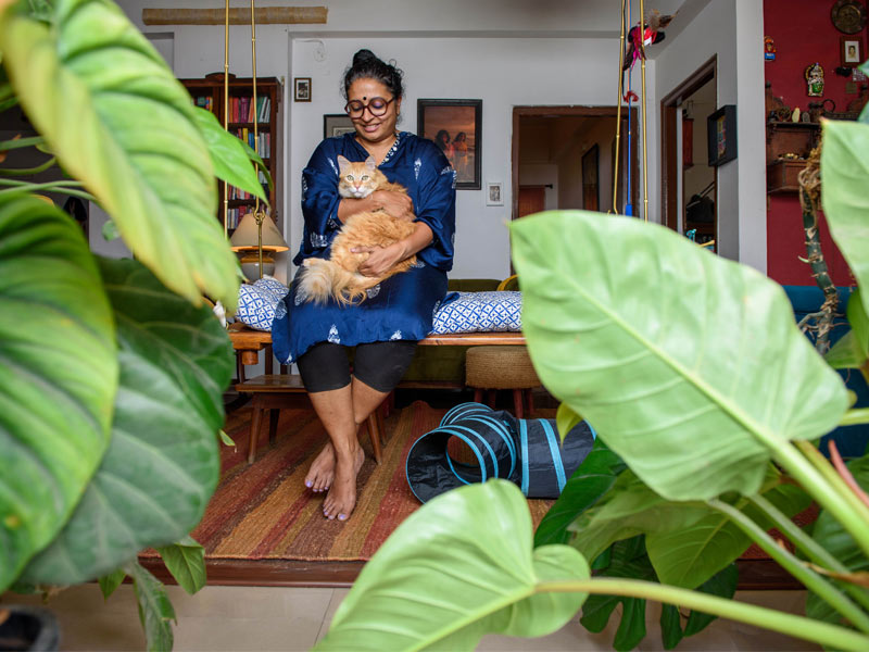 Woman Holding Ginger Cat on a Swing Surrounded by Lush Indoor Plants – Beautiful Homes