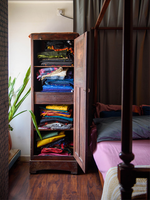 Open Wooden Cabinet with Neatly Folded Colorful Clothes Next to a Four-Poster Bed – Beautiful Homes