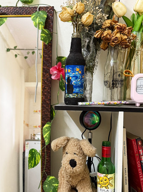 Cozy corner décor with dried flowers in glass bottles, a decorative mirror, hand-painted bottle art, plush dog toy, and books – Beautiful Homes