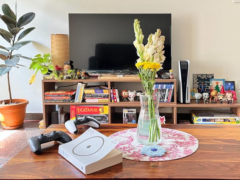 Modern living room with TV, PlayStation 5, game controllers, bookshelf décor, indoor plants, and fresh flowers on a wooden table – Beautiful Homes