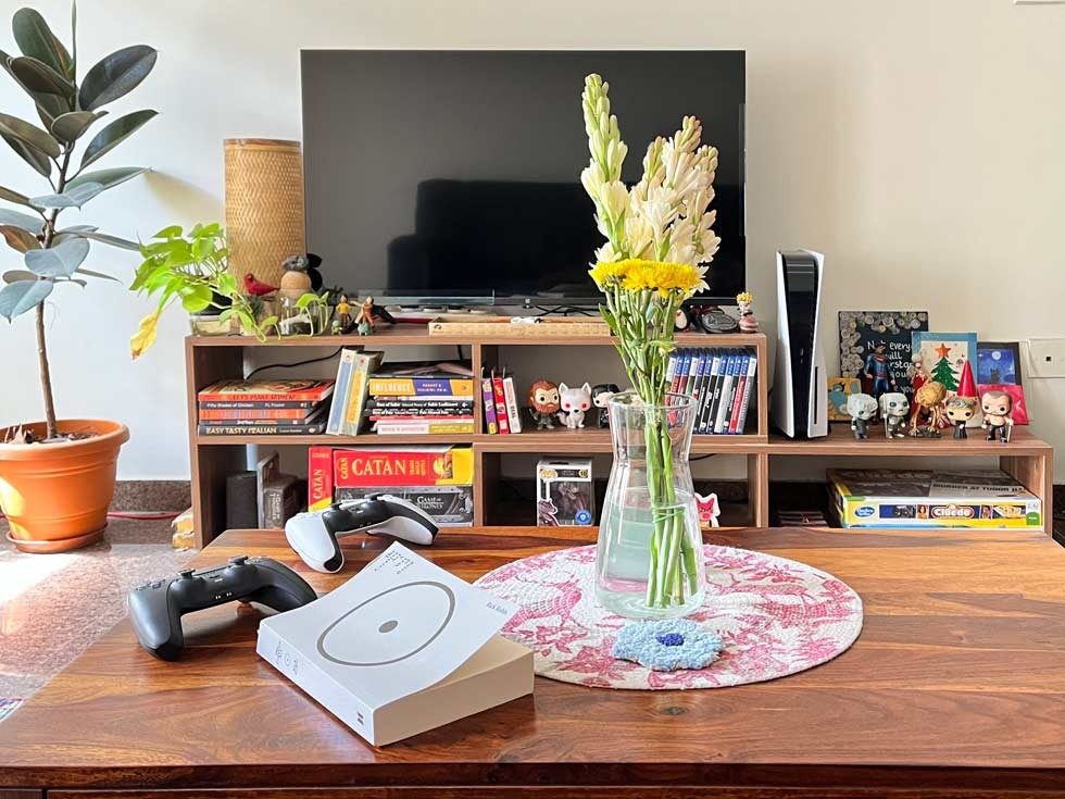 Modern living room with TV, PlayStation 5, game controllers, bookshelf décor, indoor plants, and fresh flowers on a wooden table – Beautiful Homes