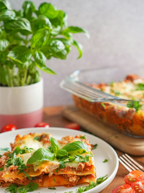 Homemade lasagna garnished with fresh basil, served with potted basil in the background – Beautiful Homes