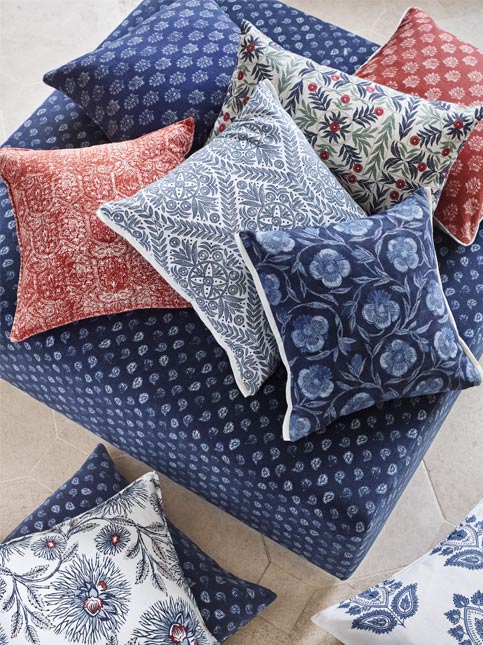 A variety of colorful decorative pillows in different patterns and textures arranged on a blue upholstered surface - Beautiful Homes