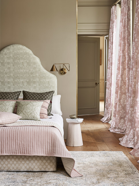 A beautifully styled bedroom featuring a headboard, soft pink bedding, decorative pillows, and flowing floral curtain - Beautiful Homes