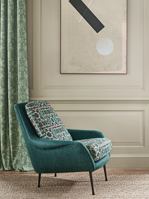 A stylish teal armchair with a patterned cushion, positioned next to a window with patterned curtains - Beautiful Homes