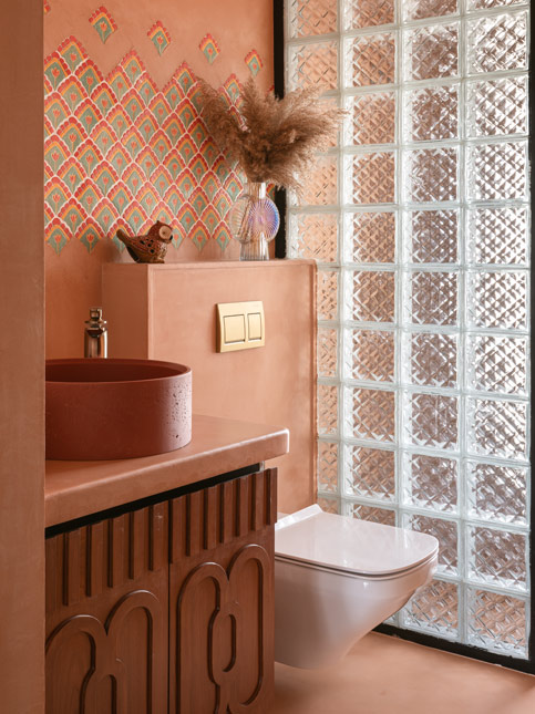 A powder bathroom with orange-pink walls, a round basin, and a partition made of glass bricks - Beautiful Homes