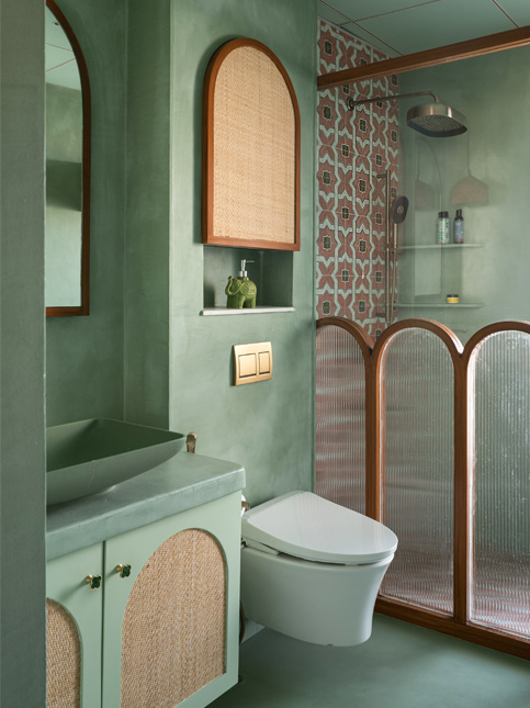 A master bathroom with green tiled walls, a toilet, and a shower area separated by a curved screen with wicker and fluted glass details - Beautiful Homes