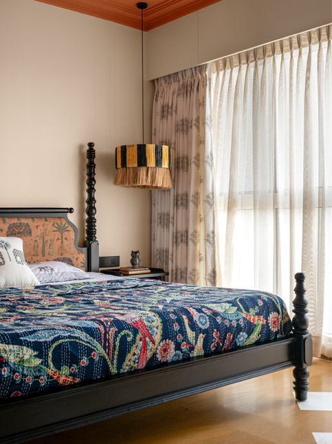 A bedroom with a dark wood bed, a colourful floral and a lampshade hanging beside the bed - Beautiful Homes