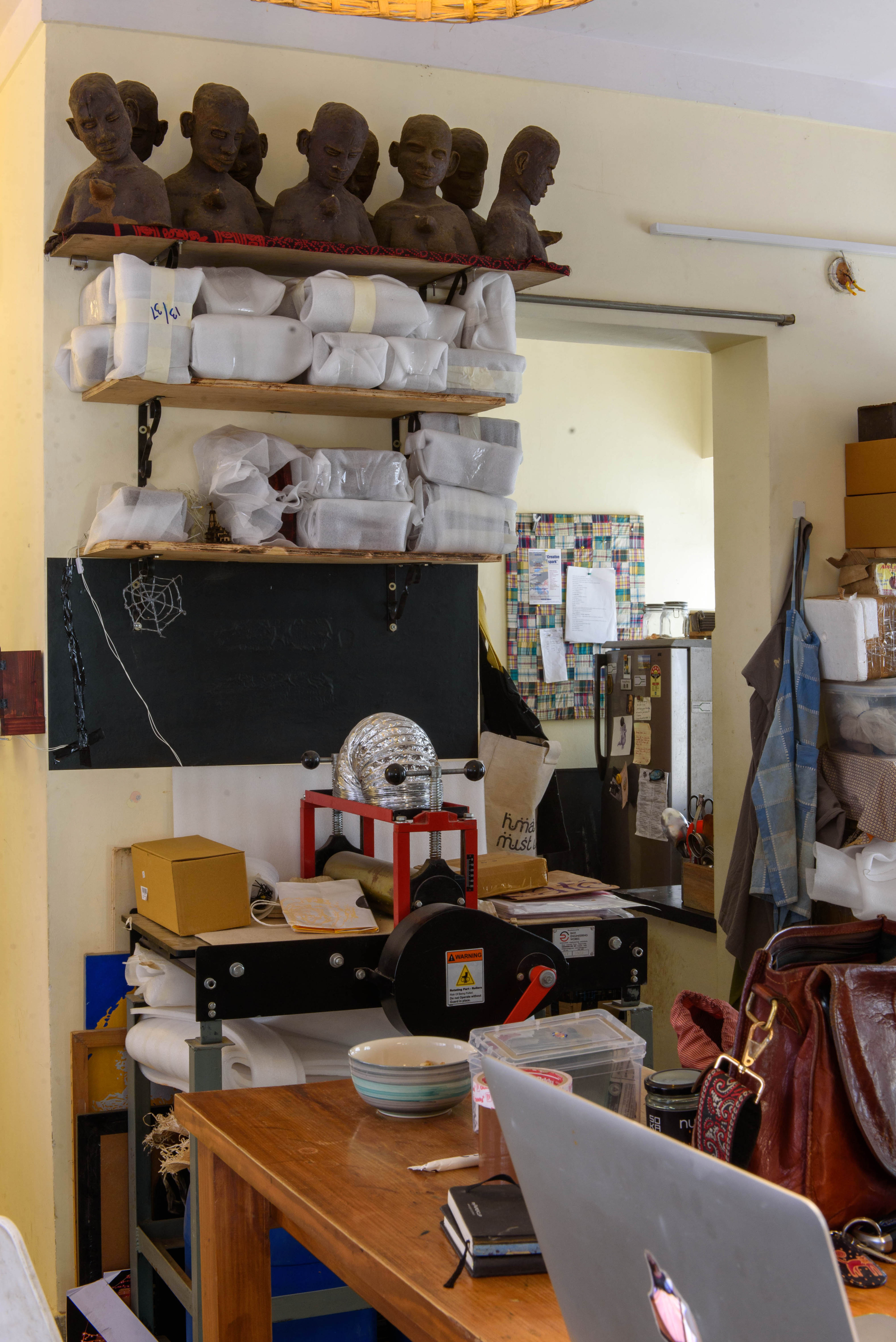 A cluttered workspace featuring shelves with busts and wrapped items, a blackboard, and various tools and boxes – Beautiful Homes