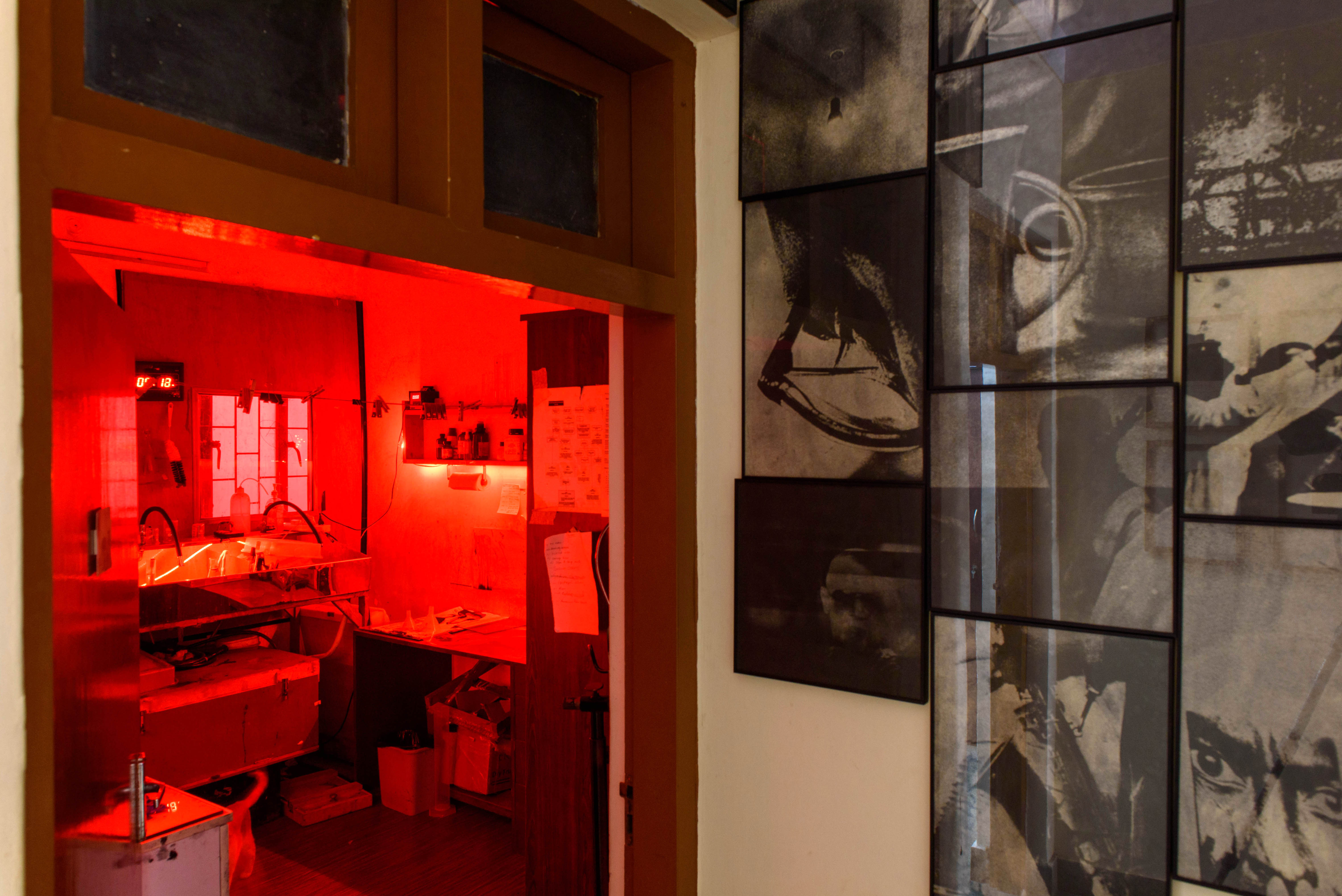 A darkroom bathed in red light, with a sink and equipment visible, next to a wall adorned with framed black and white photographs – Beautiful Homes
