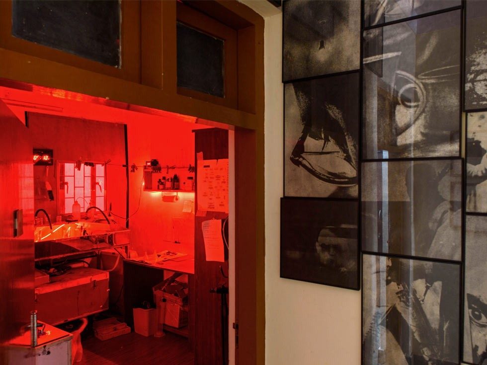 A darkroom bathed in red light, with a sink and equipment visible, next to a wall adorned with framed black and white photographs – Beautiful Homes
