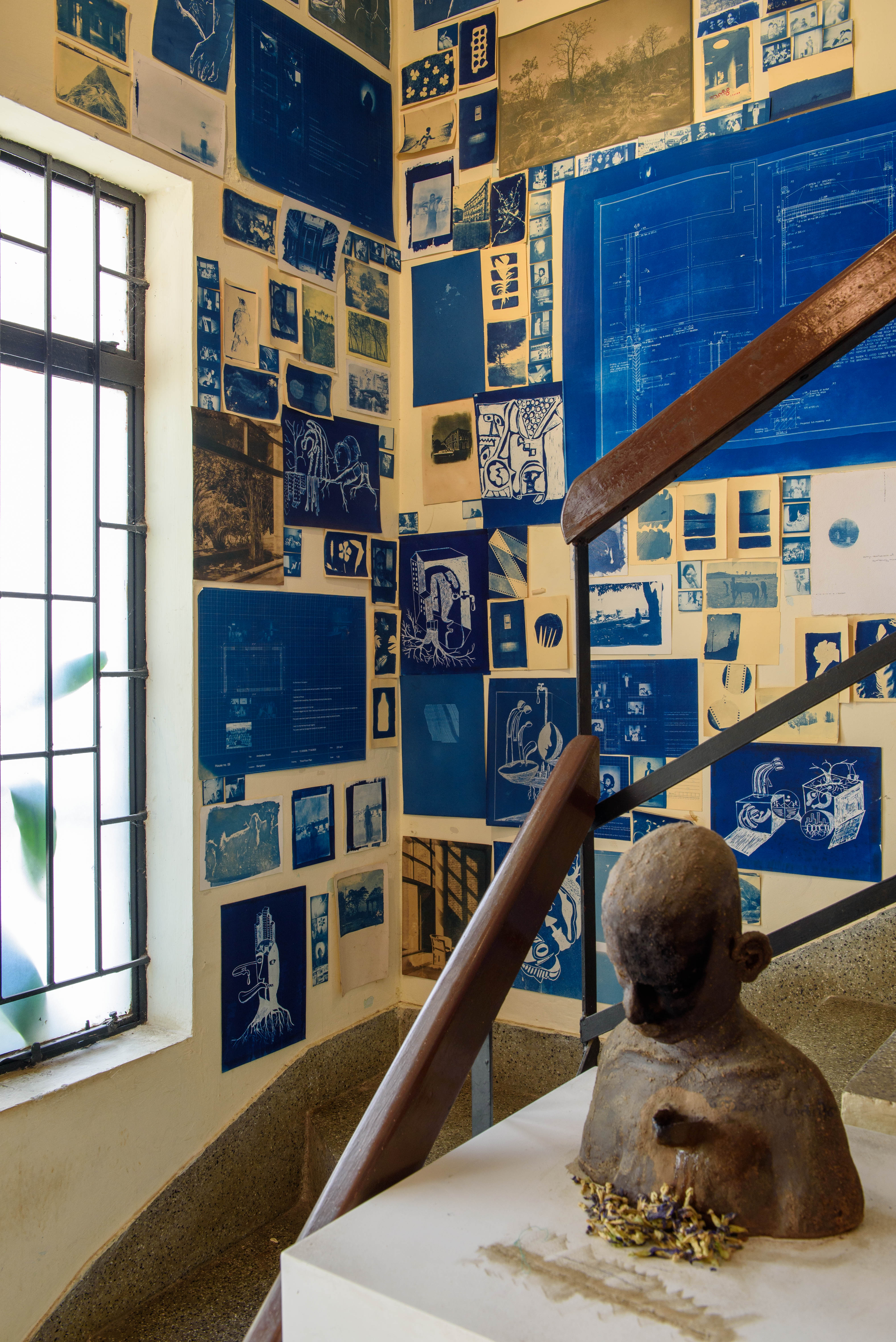A wall covered in various blue and white artworks and blueprints, alongside a small bust sculpture on a staircase landing – Beautiful Homes