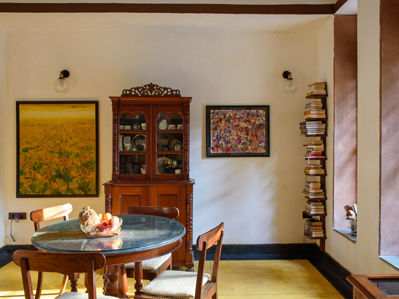 A corner of a dining room with a glass topped wooden table, a vintage wooden cabinet, and two framed pictures on the wall - Beautiful Homes
