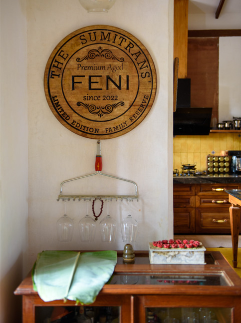 A detailed shot of a custom "Feni" sign mounted on a wall. Below it, a hanging rack holds wine glasses and a string of beads - Beautiful Homes