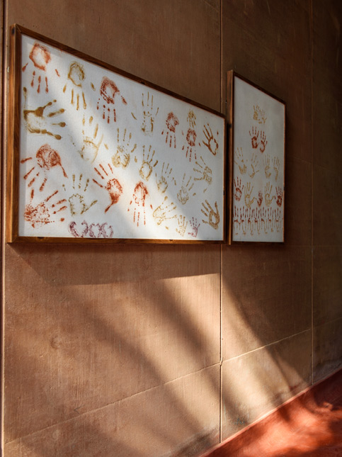 A close-up shot of two framed paintings of handprints hanging on a textured, reddish-brown wall - Beautiful Homes