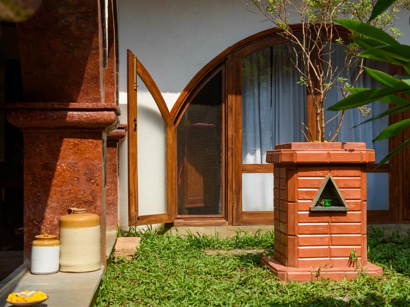 A section of a house exterior with a red brown textured pillar, a brown arched window, and an intricate terracotta planter box - Beautiful Homes