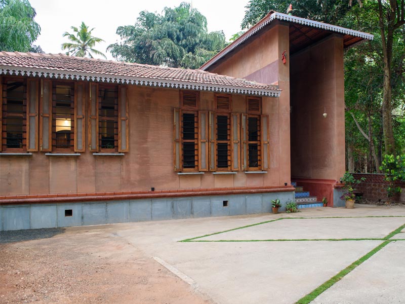An exterior view of a rustic, traditional Indian house with a clay tiled roof and red-coloured walls - Beautiful Homes