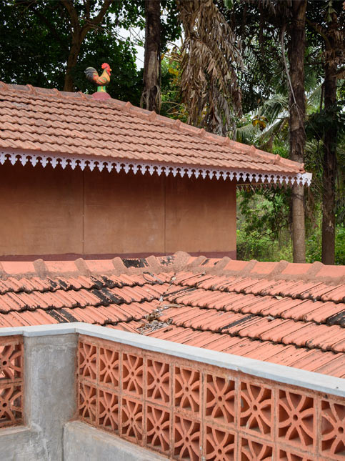 Terracotta tile roof of a house, a decorative ceramic rooster on the peak, and a concrete railing with circular patterns - Beautiful Homes