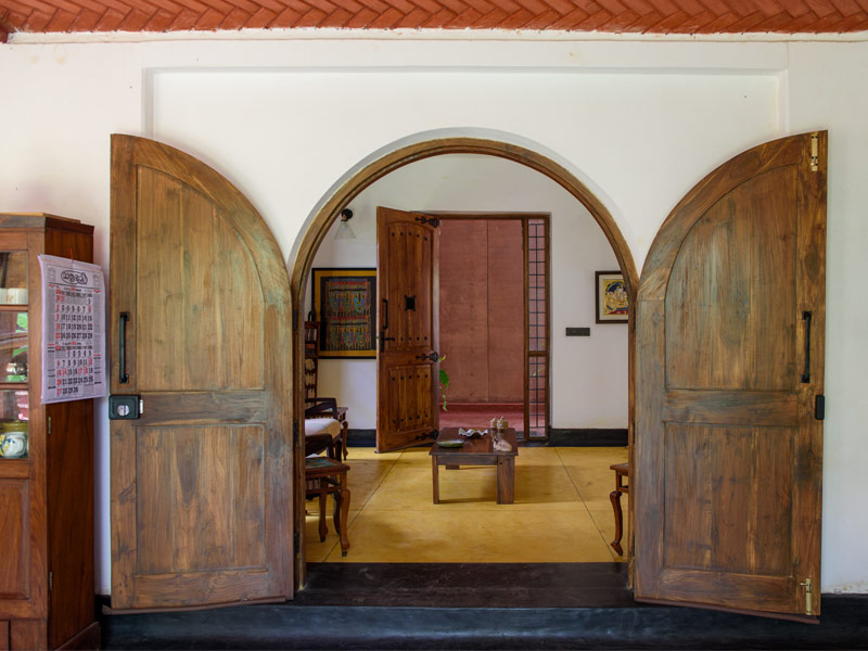 A wide shot of a traditional Indian home interior, looking through a pair of large, open wooden doors - Beautiful Homes