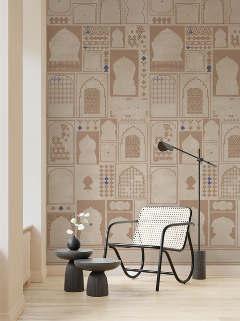 A Secret World wallpaper in a beige colourway, with a dark sofa and pink cushions, creating a stylish and inviting room – Beautiful Homes