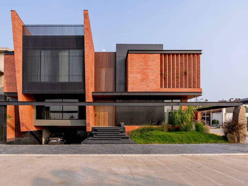Exterior view of a brick and metal home in Indore with raw stone wall accents and natural textures – Beautiful Homes