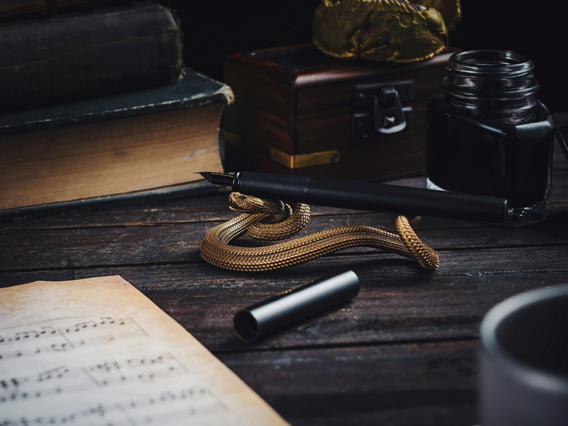 A black fountain pen rests on a coiled brass snake next to sheet music – Beautiful Homes