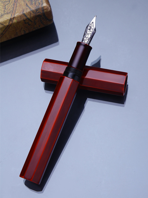 A red, faceted fountain pen with its cap off, displaying the intricate silver nib – Beautiful Homes